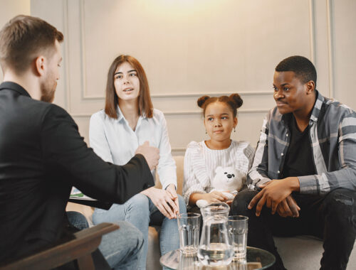 Family counseling session at home with therapist. Pshycologist showing pictures of emotions to a girL.African American father and European mother.